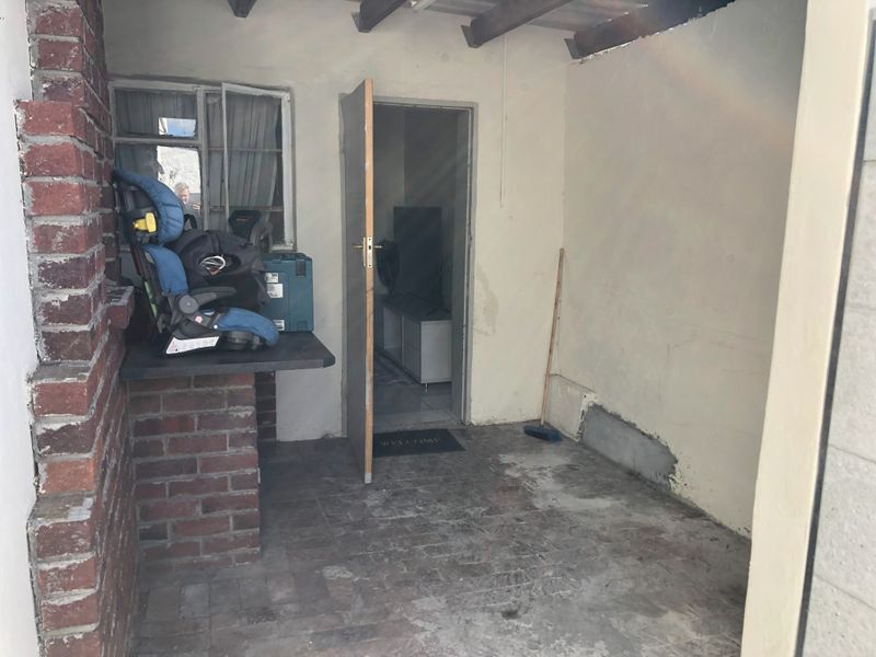A covered outdoor patio area featuring exposed timber rafters, brick paving, and a brick pillar, currently in need of maintenance and cosmetic updates.
