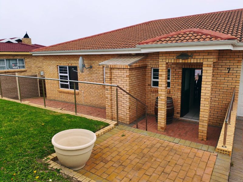 Front entrance of a face brick house featuring a tiled roof, paved patio area, and stainless steel balustrade railing.