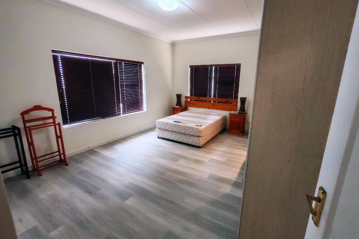 A spacious bedroom featuring modern laminate flooring, neutral walls, and large windows fitted with dark venetian blinds.