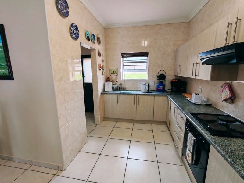 A functional kitchen featuring light wood cabinetry, granite countertops, tiled walls, and integrated cooking appliances, including an electric hob and oven.