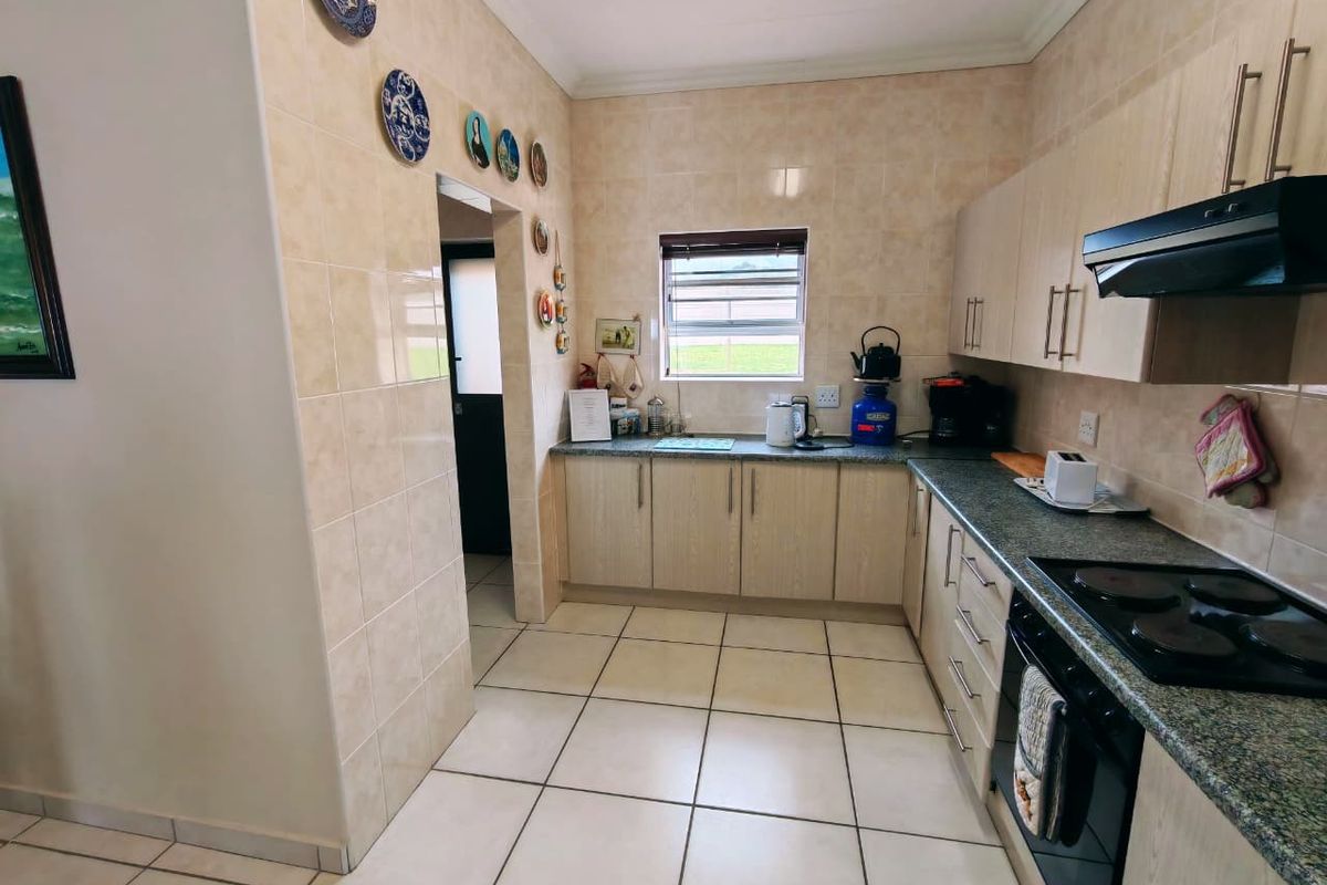 A functional kitchen featuring light wood cabinetry, granite countertops, tiled walls, and integrated cooking appliances, including an electric hob and oven.