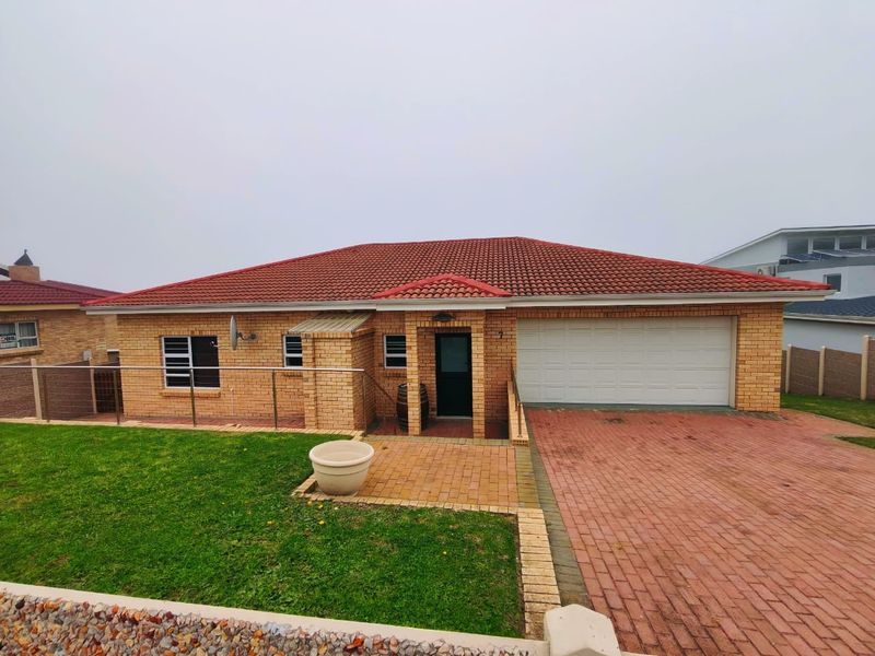 Front view of a face brick house featuring a tiled roof, paved driveway, double garage, and a neat front garden with a glass balustrade.