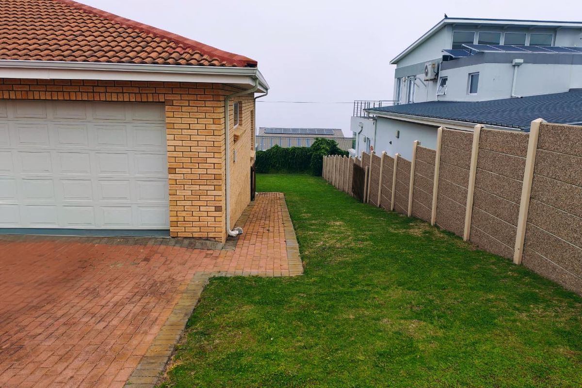 Side view of the property showing a brick garage, paved driveway, and a well-maintained lawn bordered by a precast concrete boundary wall.