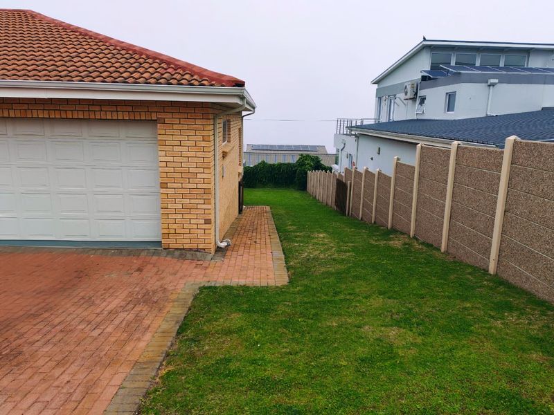Side view of the property showing a brick garage, paved driveway, and a well-maintained lawn bordered by a precast concrete boundary wall.