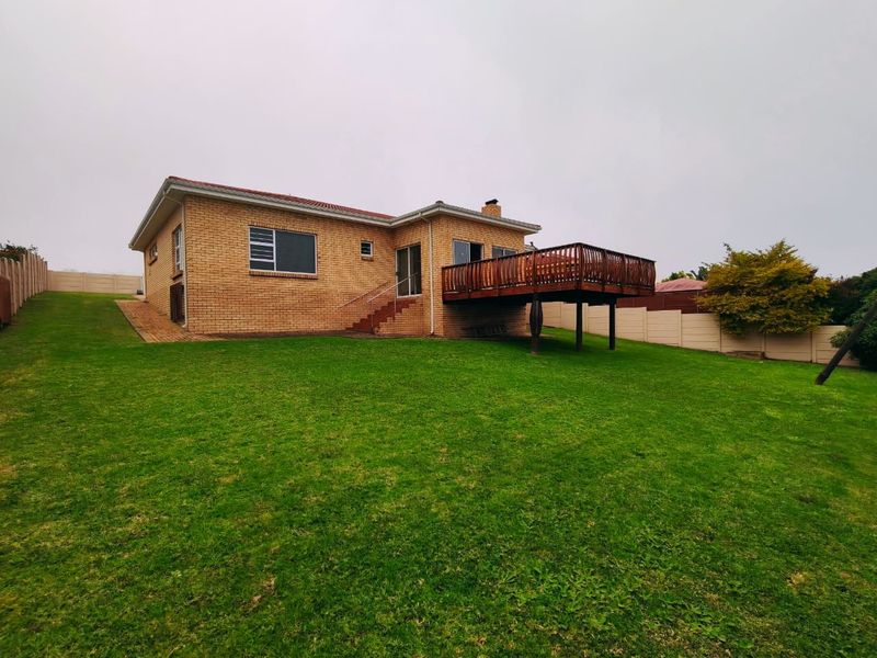 Rear view of a brick house featuring a raised wooden deck, sliding glass doors, and a spacious backyard enclosed by a boundary wall.