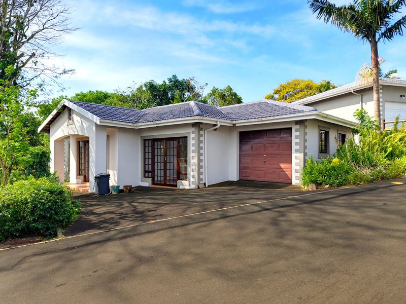Front elevation of a single-story house featuring a tiled roof, integrated garage, and paved driveway with established garden surroundings.