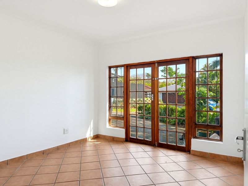 A bright, empty living area featuring tiled flooring and wooden french doors that provide direct access to the exterior.
