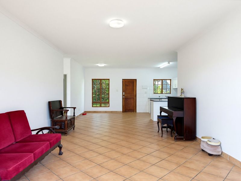 Spacious open-plan living area featuring tiled flooring, neutral walls, and an integrated kitchen space with wooden window frames and direct exterior access.