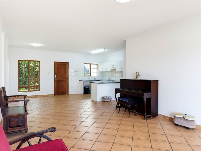Spacious open-plan living area featuring tiled flooring, neutral walls, and an integrated kitchen with white cabinetry and functional workspace.