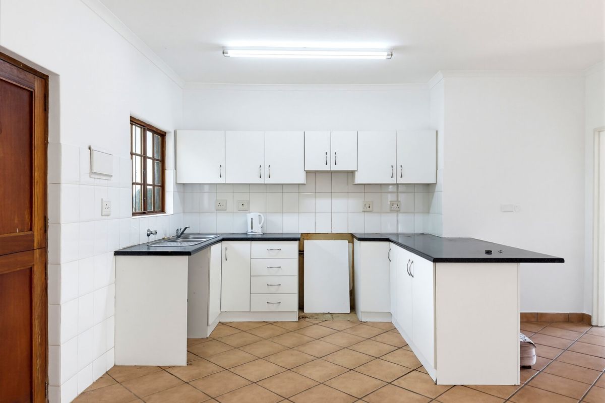 A functional, empty kitchen featuring white cabinetry, dark countertops, tiled splashbacks, and ceramic floor tiles, offering a blank canvas for modern updates.