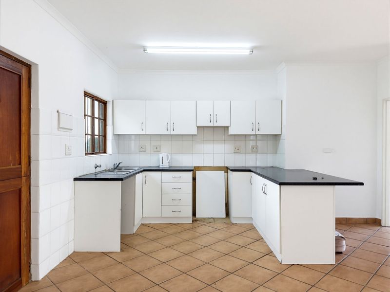 A functional, empty kitchen featuring white cabinetry, dark countertops, tiled splashbacks, and ceramic floor tiles, offering a blank canvas for modern updates.