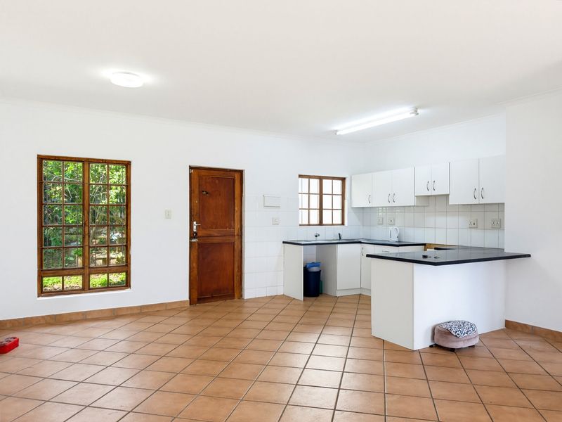 Open-plan kitchen and living area featuring tiled flooring, built-in cabinetry with laminate countertops, and timber-framed windows overlooking the garden.