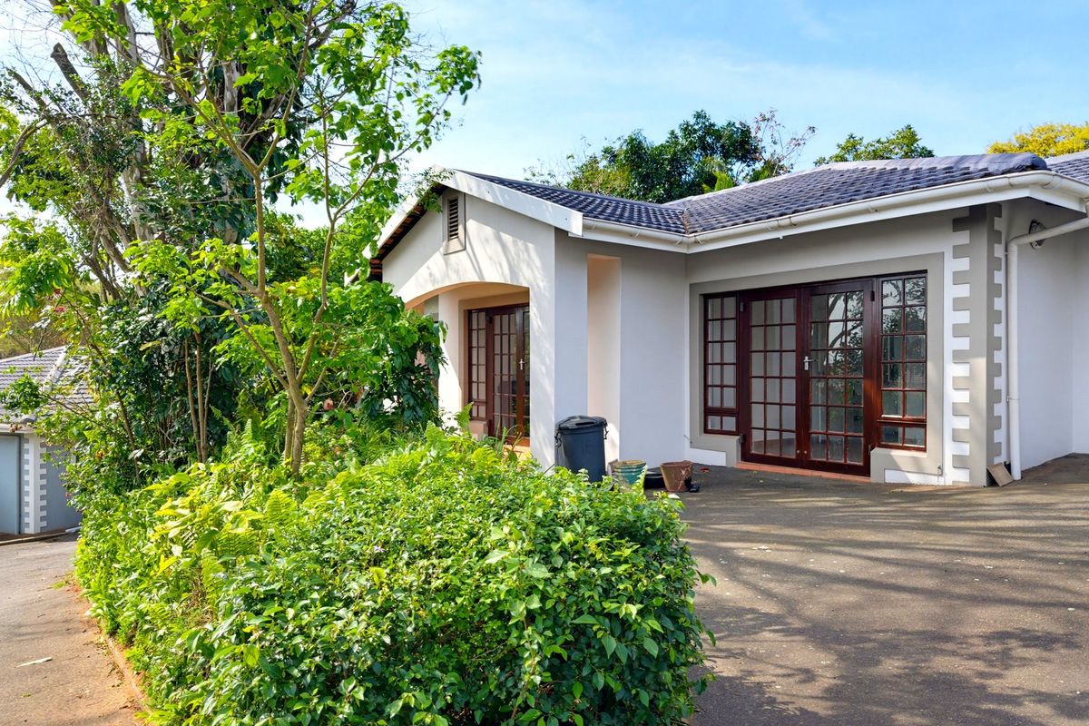 A rear view of the house featuring a paved patio area, timber-framed glass doors, and a well-maintained tiled roof.
