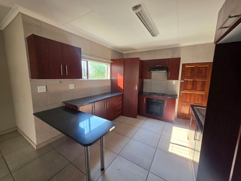 A functional kitchen featuring dark wood cabinetry, granite countertops, built-in oven and hob, and tiled flooring, offering a clean and practical workspace.