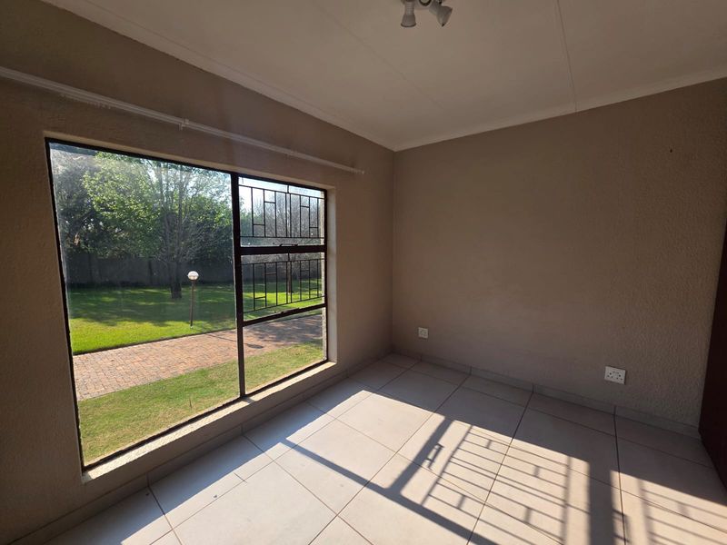 A bright, empty bedroom featuring tiled flooring, a large window with security bars, and neutral wall finishes, offering a clean canvas for personalization.