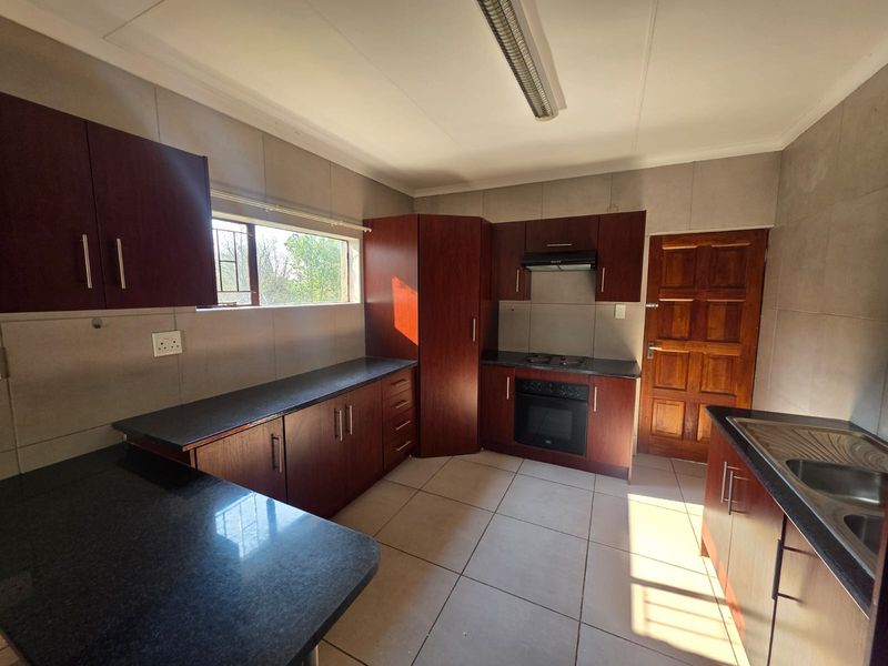 A functional kitchen featuring dark wood cabinetry, granite countertops, built-in oven, hob, extractor fan, and tiled finishes throughout.
