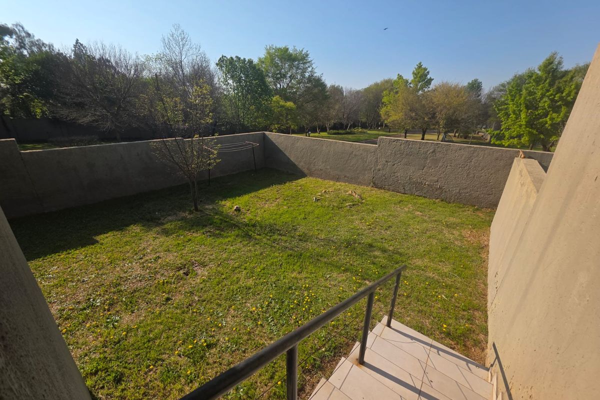 A private rear garden area featuring a lawn, enclosed by high boundary walls, with a tiled staircase and metal handrail leading down from the property.