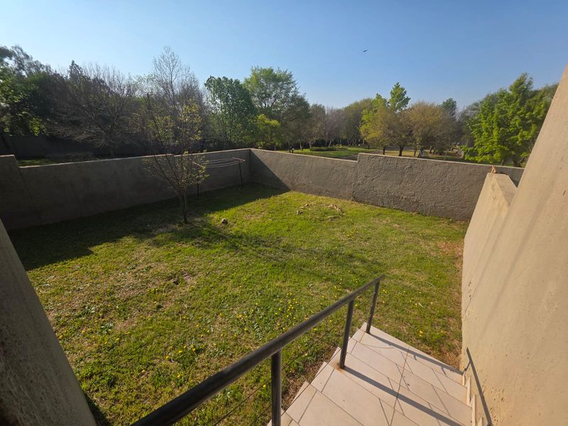 A private rear garden area featuring a lawn, enclosed by high boundary walls, with a tiled staircase and metal handrail leading down from the property.