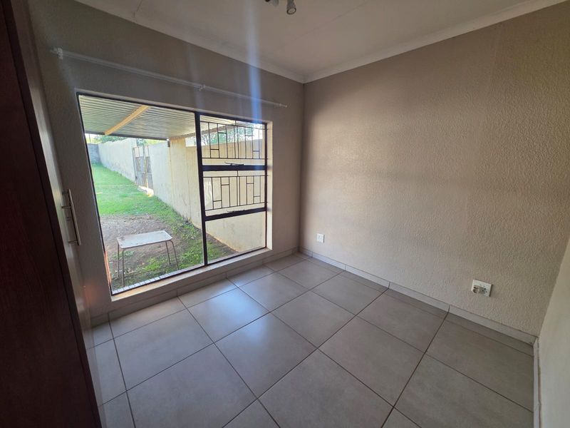An empty bedroom featuring tiled flooring, a built-in cupboard, and a large window with security bars overlooking the rear garden area.