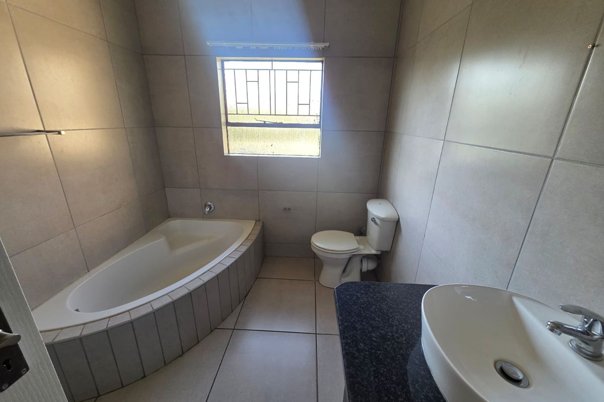 A clean, tiled bathroom featuring a built-in corner bathtub, a modern vanity basin with a granite countertop, and a toilet.