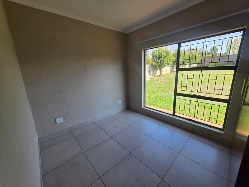 An empty bedroom featuring neutral tiled flooring, a large window with security bars, and views overlooking the rear garden.