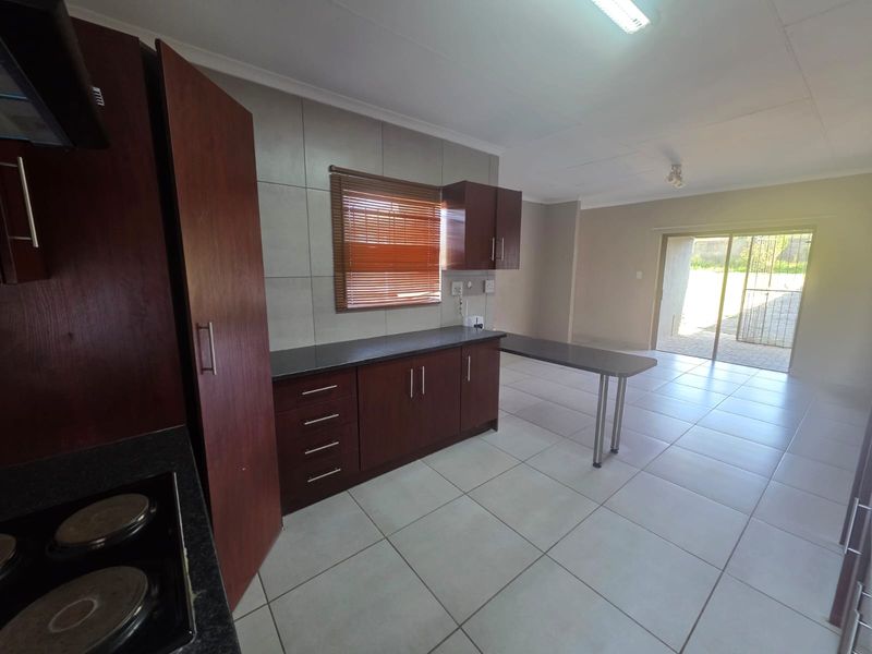 Open-plan kitchen and living area featuring dark wood cabinetry, granite countertops, tiled flooring, and direct access to the rear patio through sliding glass doors.