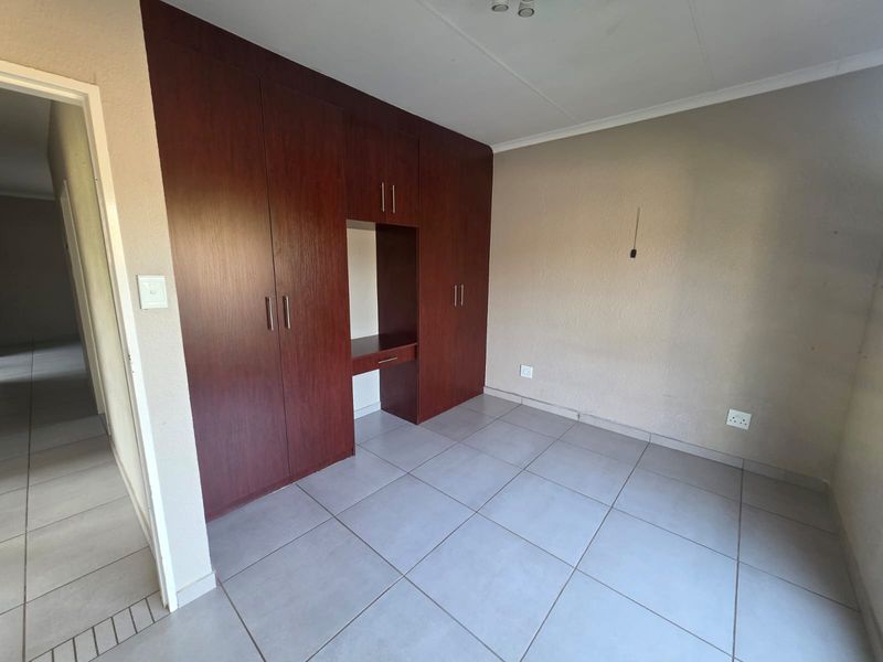 A clean, empty bedroom featuring neutral tiled flooring and extensive dark wood built-in cupboards with an integrated desk space.
