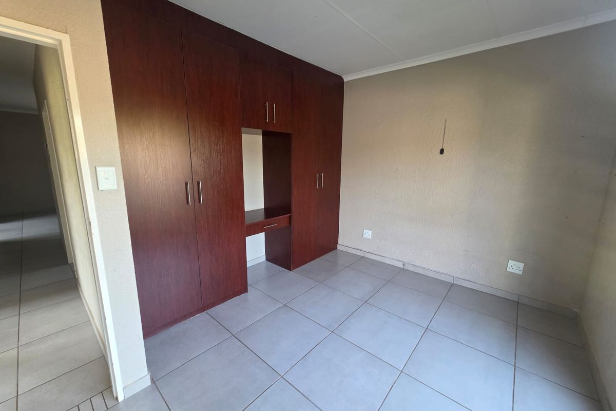 A clean, empty bedroom featuring neutral tiled flooring and extensive dark wood built-in cupboards with an integrated desk space.