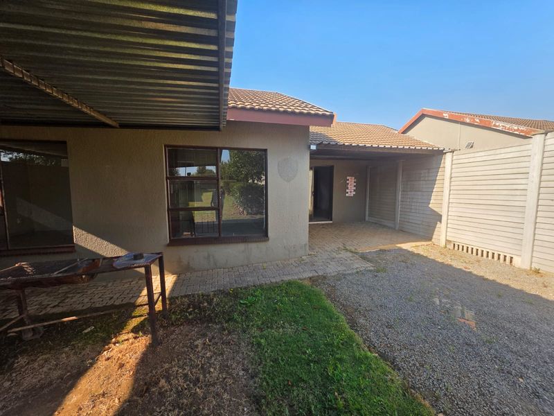 Rear exterior view of the townhouse featuring a paved patio area, corrugated metal roofing, and a gravel driveway enclosed by a precast concrete boundary wall.