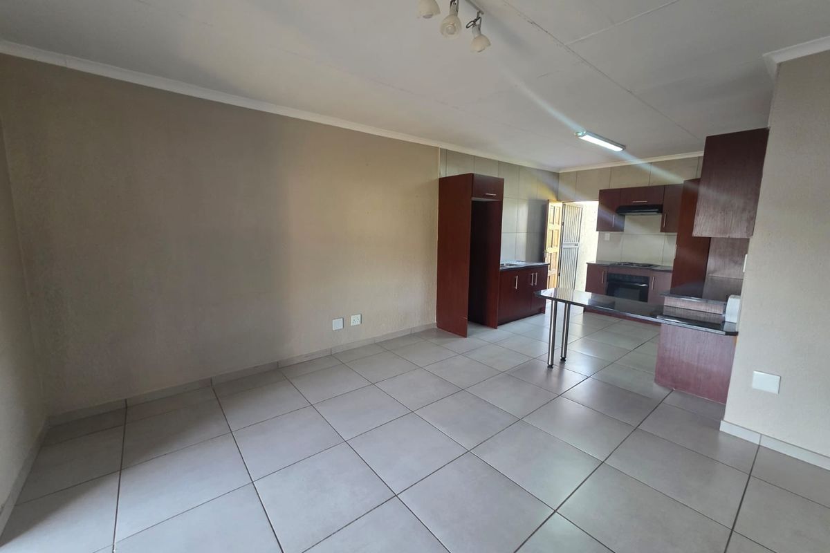 Open-plan living and kitchen area featuring tiled flooring, built-in cabinetry, and a breakfast counter, offering a functional and versatile space.