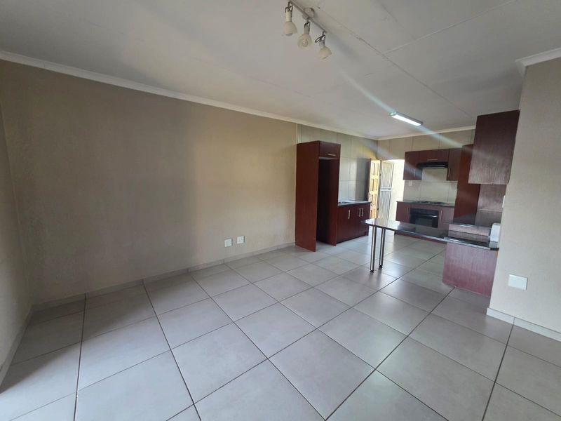 Open-plan living and kitchen area featuring tiled flooring, built-in cabinetry, and a breakfast counter, offering a functional and versatile space.