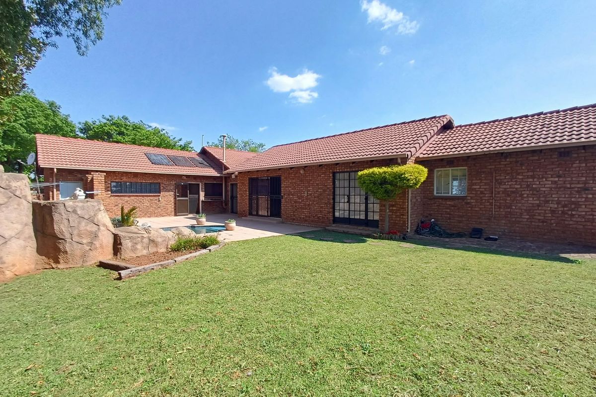 Spacious rear garden featuring a brick-clad home, a swimming pool with a decorative rock feature, and a paved patio area under a tiled roof.