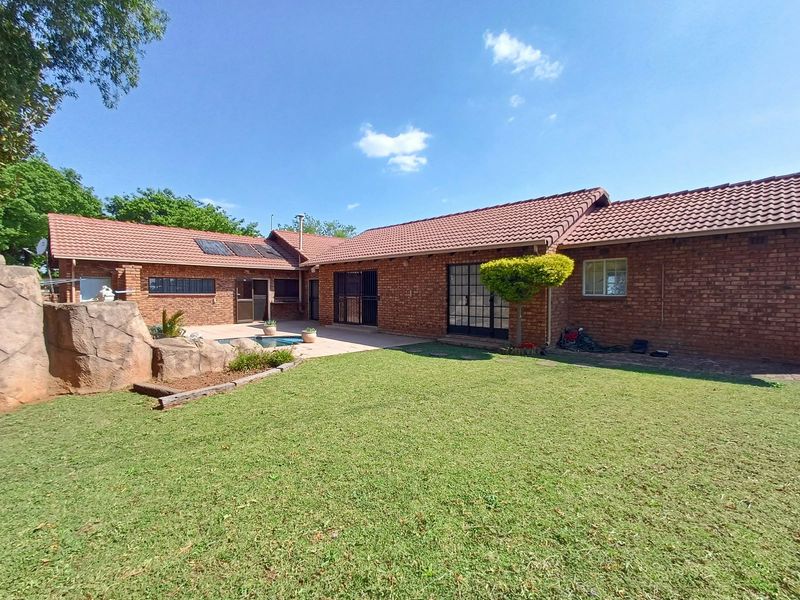 Spacious rear garden featuring a brick-clad home, a swimming pool with a decorative rock feature, and a paved patio area under a tiled roof.