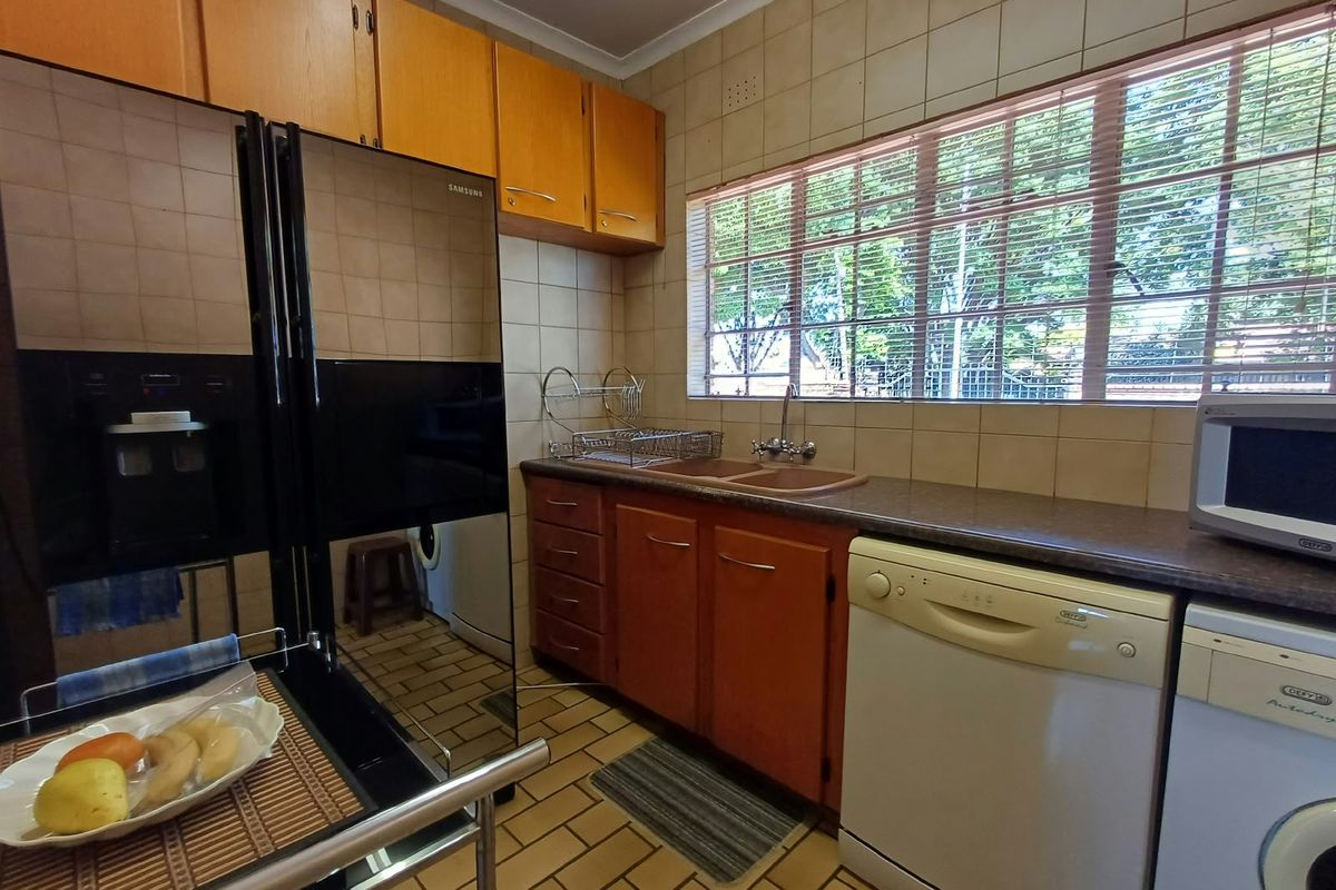 A functional kitchen featuring wooden cabinetry, laminate countertops, a double basin sink, and tiled finishes throughout.