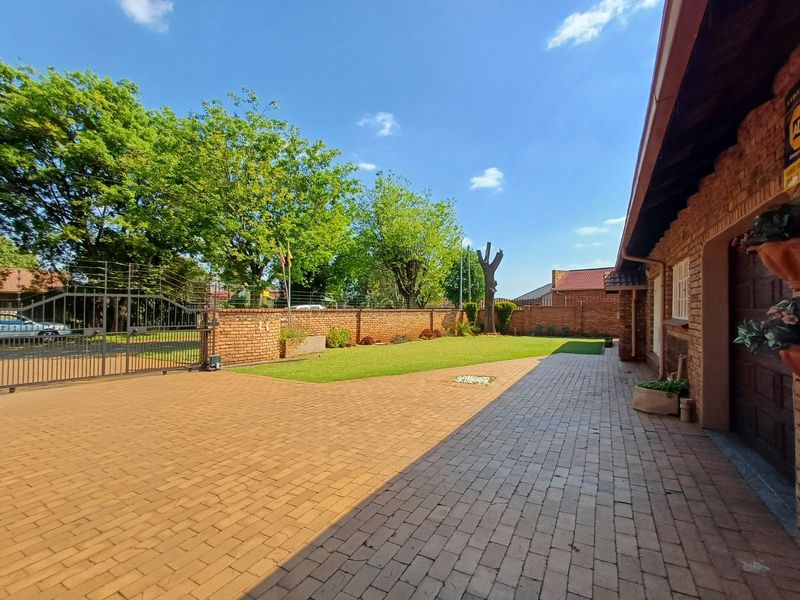 Spacious front exterior featuring a paved driveway, brick boundary wall with electric fencing, and a secure metal gate entrance.