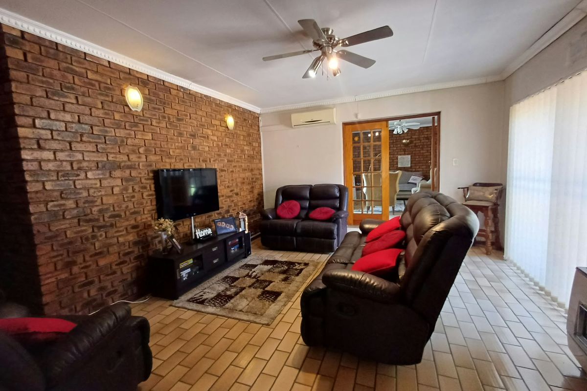 Spacious living room featuring an exposed brick feature wall, tiled flooring, ceiling fan, and split-system air conditioning with access to an adjoining room.
