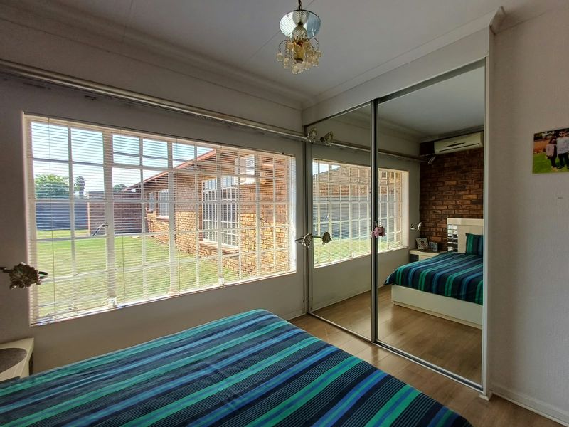 A well-lit bedroom featuring laminate flooring, a large built-in mirrored wardrobe, an exposed brick feature wall, and a split-system air conditioner.