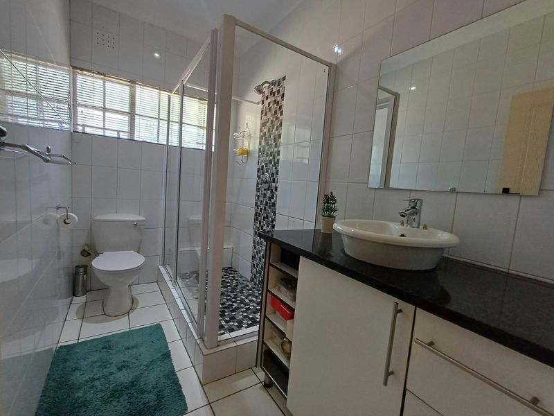 A functional bathroom featuring a glass-enclosed shower with mosaic accents, a vanity with a granite countertop, and white wall tiling.