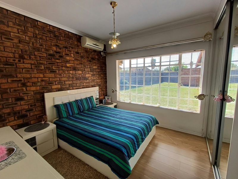A well-maintained bedroom featuring an exposed brick feature wall, laminate flooring, built-in sliding wardrobes, and a split-system air conditioner.