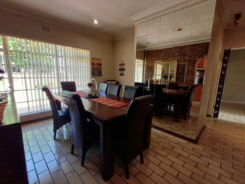 Dining room featuring tiled flooring, a large mirrored wall accent, exposed brickwork, and natural light through vertical blinds.