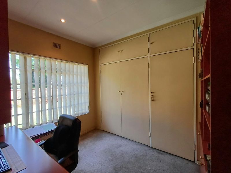 A bedroom featuring built-in cupboards, carpeted flooring, and vertical blinds, providing a functional space with neutral finishes.