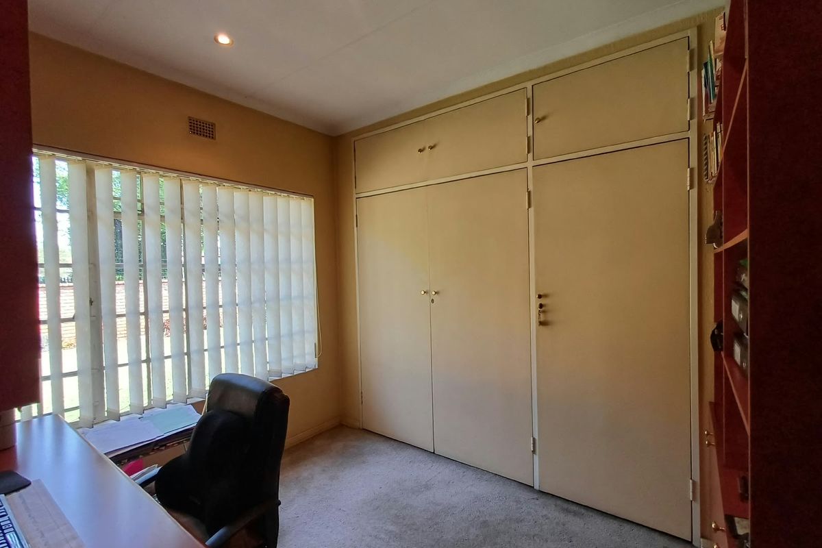 A bedroom featuring built-in cupboards, carpeted flooring, and vertical blinds, providing a functional space with neutral finishes.