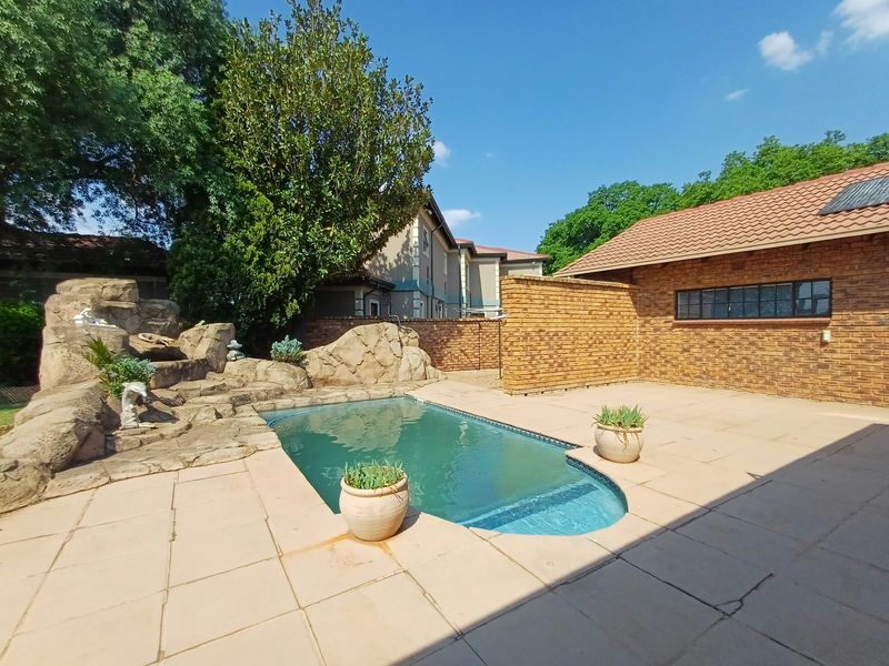 Outdoor pool area featuring a rock water feature, brick boundary walls, and paved patio space.