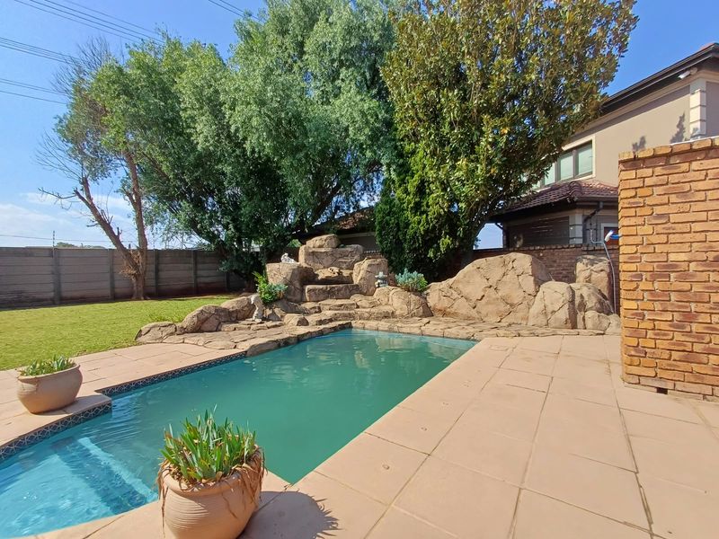 Outdoor pool area featuring a natural rock water feature, paved decking, and established garden surroundings.