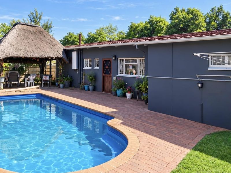 Outdoor pool area featuring a paved patio, a traditional thatched lapa, and well-maintained exterior finishes.