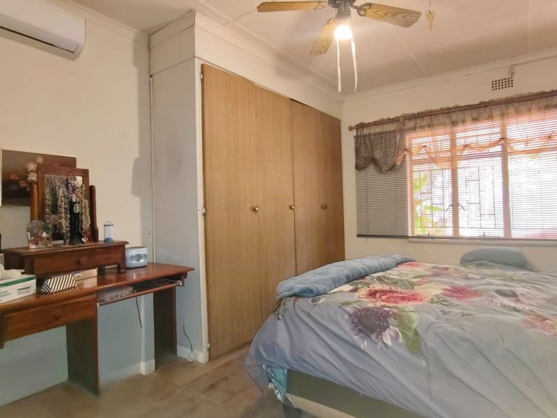 A bedroom featuring a built-in wardrobe, ceiling fan, and split-system air conditioning unit, with security bars installed on the window.
