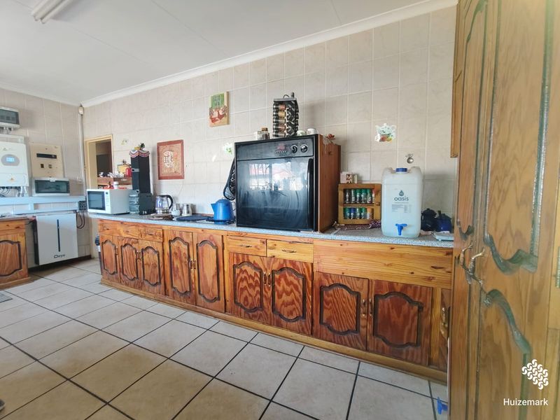 A functional kitchen featuring extensive wooden cabinetry, tiled splashbacks, and tiled flooring, equipped with a built-in oven and wall-mounted gas geyser.