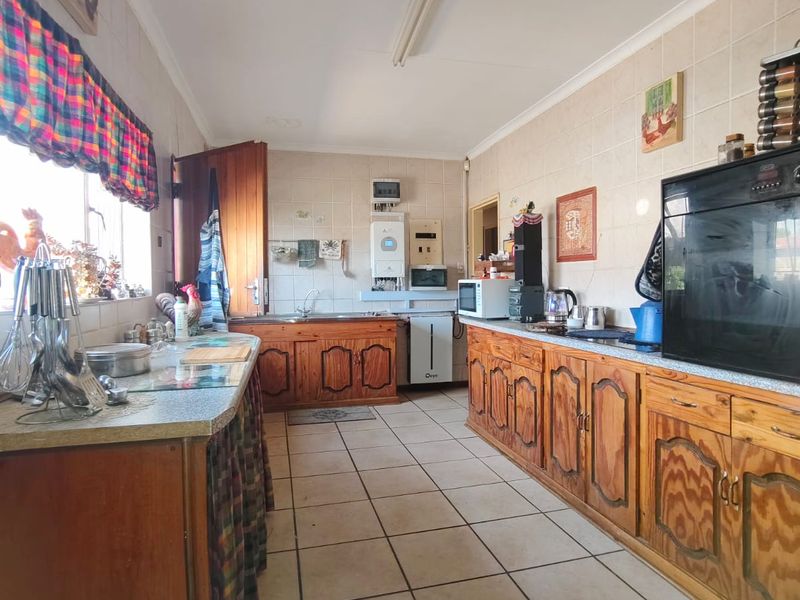 A functional kitchen featuring extensive wooden cabinetry, tiled walls and flooring, a built-in oven, and a gas geyser for water heating.