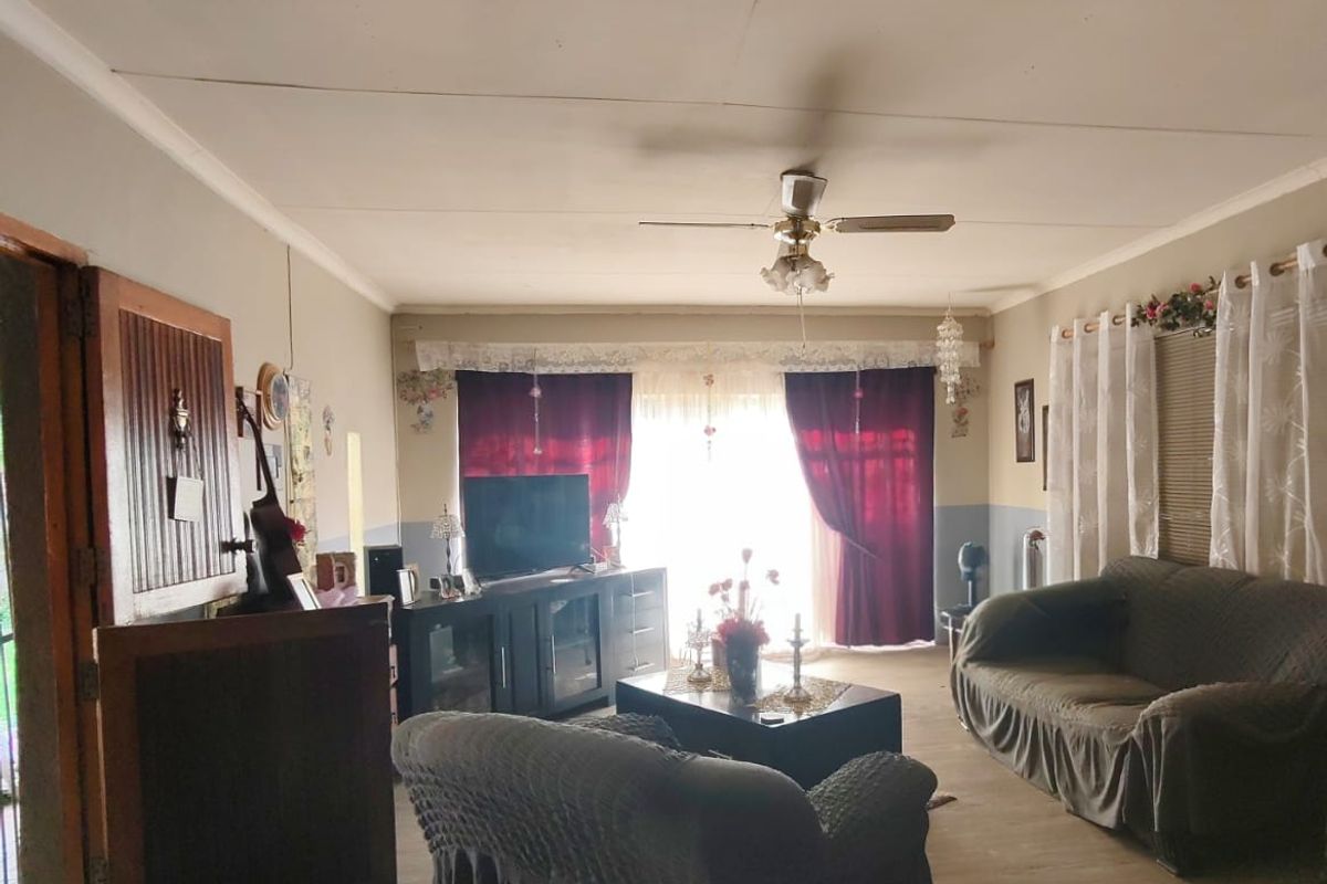 A spacious living room featuring laminate flooring, a ceiling fan, and natural light through large windows, offering a comfortable and functional living space.