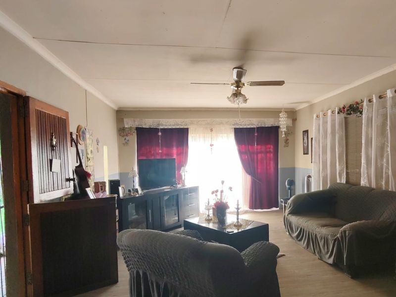 A spacious living room featuring laminate flooring, a ceiling fan, and natural light through large windows, offering a comfortable and functional living space.